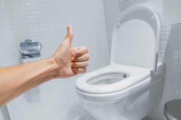 Hand gesturing thumbs up in a clean and modern bathroom with white toilet, showing satisfaction for plumbing and hygiene