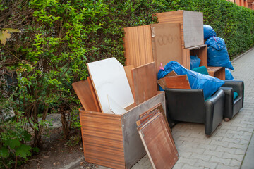 Discarded furniture, wooden panels, and blue trash bags on a sidewalk. Urban waste collection or...