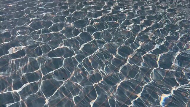 Sunlight reflecting on water surface in swimming pool with visible tile pattern. Abstract background texture. Summer vacation and relaxation concept. Design for wallpaper, banner, poster, header