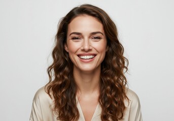 Joyful young woman with long wavy brown hair smiling brightly against a clean white backdrop