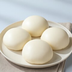Four fluffy, plain steamed buns (mantou) are presented on a white plate with a subtle clean background and napkin, ready to be enjoyed