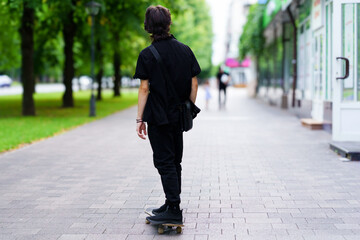 Fototapeta premium Young person skates down a city sidewalk surrounded by trees in daylight