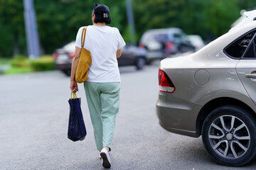 Person walking with a bag in a parking lot during daytime near parked cars © Nariman