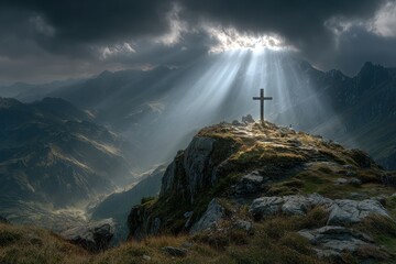Cross silhouette stands atop mountain peak during dramatic sunset with golden sunbeams shining through cloudy sky over distant mountain range