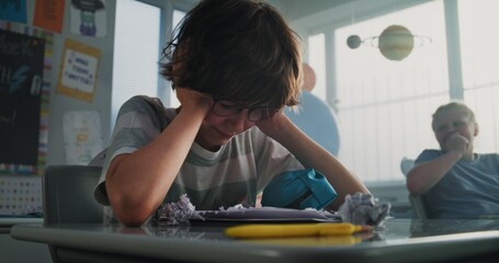 Stressed Primary School Boy Sitting Alone at Desk in Classroom While Aggressive Classmates Abusing Him, Throwing Papers and Laughing. School Bullying, Peer Harassment and Toxic School Environment.