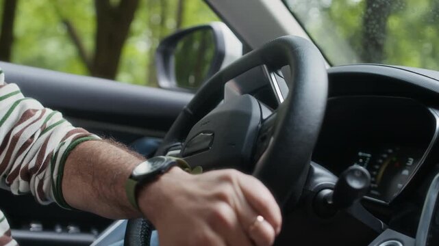 Hands of young unrecognizable male driver sitting on front seat of car and turning steering wheel after starting vehicle during summer trip on weekend