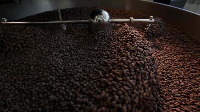 Dynamic coffee bean roasting process in industrial roaster with turning agitator arms.