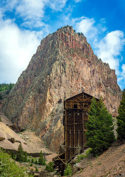 Abandoned wooden mining structure nestled beneath a towering rocky peak near Creede, Colorado, showcasing the rugged beauty of the Rocky Mountains and remnants of frontier history.