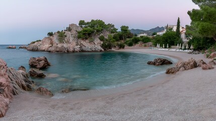 Secluded turquoise beach surrounded by rocky cliffs and pine trees under a pastel evening sky, with sun loungers in view
