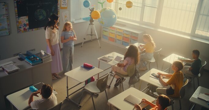STEM Class: Female Teacher Educating Ecology to Elementary School Students in Classroom. Diverse Kids Raising Hands to Give Answer, Smart Girl Going to the Board and Presenting Homework. High Angle.