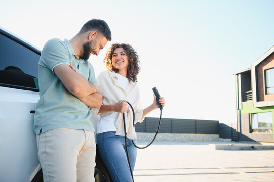 Happy couple charging electric car at home, embracing green energy and sustainable lifestyle