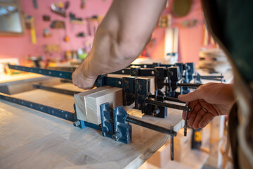 Unrecognizable woodworker hands tight clamps on beams to form solid plank in workshop. Glue apply, beam alignment, strong grip, extended drying, craftsmanship skill, sanding prepare, small business