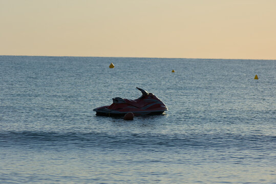 jet ski floats in calm blue water, surrounded by red and yellow buoys, with a hazy horizon in the distance.
