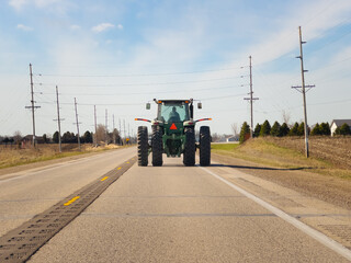 Tractor driving down a two lane asphalt road. Viewed from behind