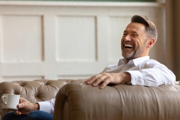 Smiling Man Laughing on Chesterfield Sofa with Coffee Cup