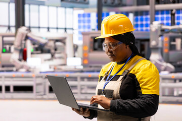 In modern facility, African american female engineer using her laptop to oversee production, ensuring efficient and safe operations. She works on creating cutting edge devices in factory.