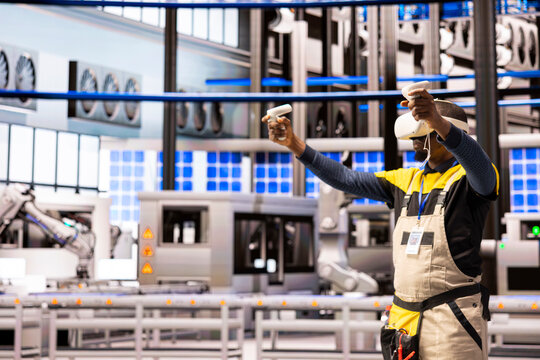 African American engineer with VR headset exploring industrial automation in smart manufacturing plant. Industry 4.0 specialist interacts with virtual reality simulation, improving system performance.