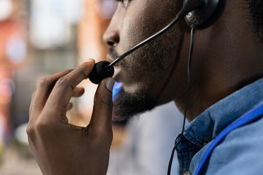 Call center agent wearing headset at office desk resolving customers concerns, talking into microphone. Close up of customer service staff member using headphones mic processing clients orders