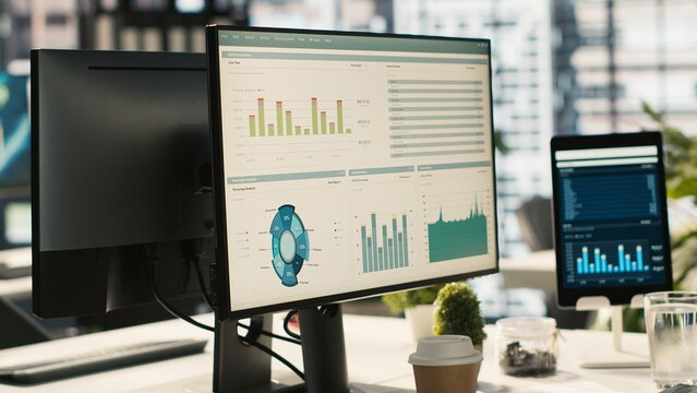 Financial charts and KPI metrics on displays in office, panning shot. Vibrant and collaborative modern workspace with computer screens displaying data analytics, close up shot
