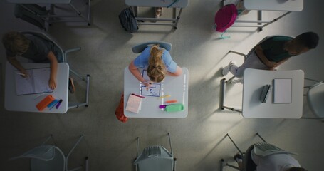 Top View on Elementary School Girl Drawing in School Notebook in Classroom. Diverse Kids Running Between Desks, Playing and Having Fun During Break Before Lesson. Interactive Learning in Modern School