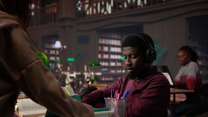 African american guy student uses ambient focus music to help with school assignment, collecting citations from books and other academic sources from the university database. Camera B.