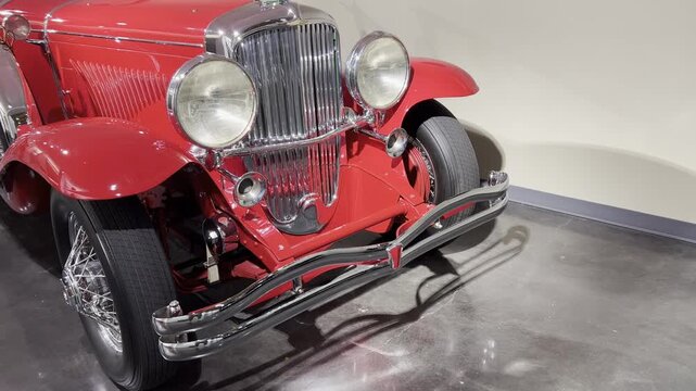 Front end of a red classic car with chrome grille, large round headlights, and shiny bumper.