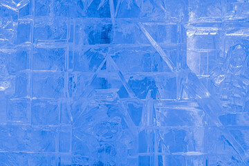 Detailed close-up of an ice wall with carved winter figures and geometric patterns. Frozen translucent texture in cold blue tones. Abstract icy background from a sculpture or ice palace in winter.