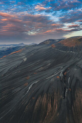 Dramatic aerial view of Iceland's volcanic terrain with ash covered slopes, reddish brown rocks,...
