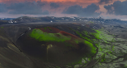 Aerial view of a volcanic Apple crater with green moss, dark soil, winding streams, and distant...