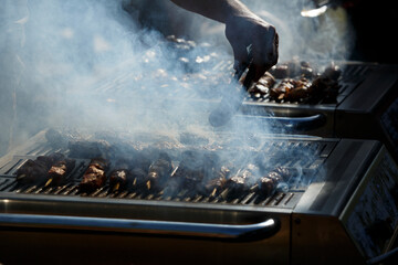 Grilling meat skewers at a vibrant outdoor barbecue gathering in a sunny park during midday