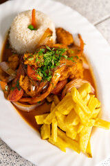 Spicy peruvian fish stew with french fries and rice on white plate