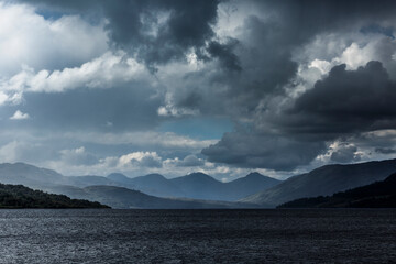 Dramatic cloud formations over the tranquil waters of a Scottish loch at dusk