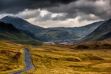 Majestic landscape of rolling mountains and winding road under overcast sky in the Scottish Highlands during late afternoon