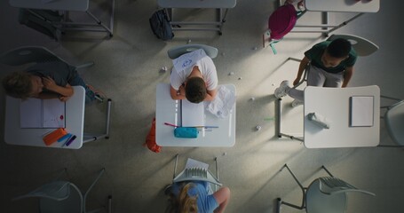 Sad Elementary School Student Sitting Alone at Desk and Crying While Classmates Bullying Him, Laughing and Throwing Papers. Boy Suffering from Peer Harassment and School Bullying. Rotating Top View.