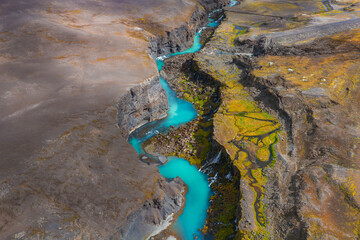 Aerial view of Sigoldugljufur Canyon in Iceland, featuring a turquoise river winding through steep rocky walls with green moss and earthy terrain.