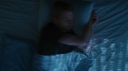 A young man lies awake in bed at night, turning restlessly due to insomnia, frustrated and exhausted, struggling with overthinking and sleep issues. Top view, time lapse - Powered by Adobe