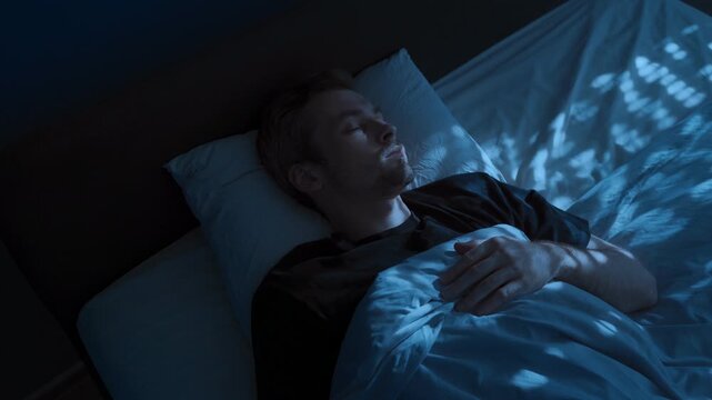 A young man wakes up tense and exhausted in bed at night, suffering from insomnia and a sleep disorder, covering his face with his hand. Sleep paralysis or nightmares