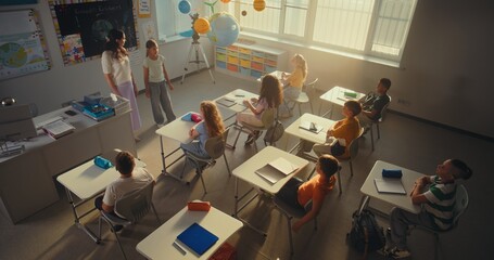 Obraz premium Female Teacher Teaching Kids During Environmental Science Lesson in Modern Classroom. Smart Children Raising Hands, Primary School Girl Showcasing Knowledge of Ecology in Front of Class. High Angle.