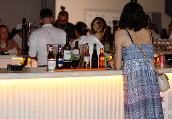 Mujer de noche pidiendo bebida a camareros entre botellas en la barra de un bar terraza tipo pub de copas nocturno