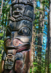 Weathered totem pole featuring detailed carvings, showcasing cultural heritage amid lush northwestern forest landscape