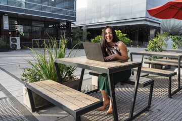 Cheerful businesswoman working on laptop outdoors in urban setting