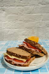 Two natural ham and cheese sandwiches on multigrain bread with fresh juice