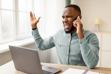 Angry Black Businessman Talking On Phone Shouting Calling To Customers Support Hotline Having Problem Sitting At Workplace In Modern Office. Displeased Customer, Corporate And Communication Issue