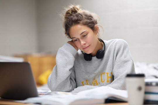 Young woman studying, wearing headphones, with laptop and book. Ideal for illustrating education, online learning, student life, concentration, or thoughtful moments.