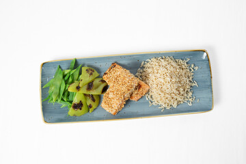 Grilled salmon in sesame crust with rice and green vegetables on a plate on a white background