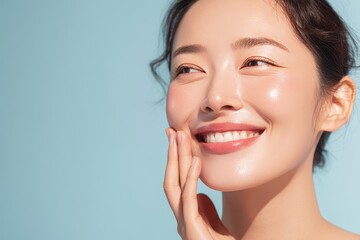 Obraz premium Portrait of a cheerful Asian woman with glowing skin featuring natural makeup against a blue backdrop showcasing beauty and skincare