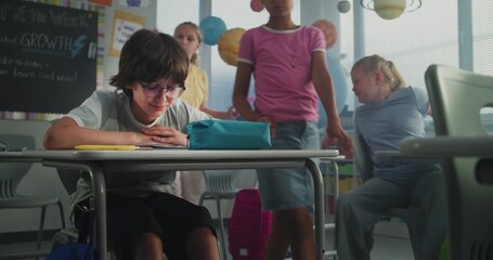 Depressed Primary School Boy Sitting Alone at Desk in Classroom While Aggressive Classmates Abusing Him, Throwing Papers and Laughing. School Bullying, Peer Harassment and Toxic School Environment.