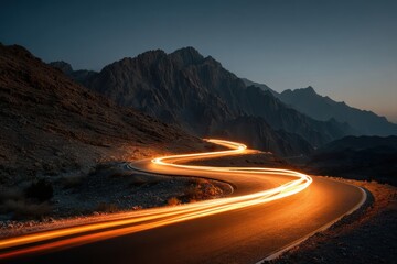 Light trails on the winding mountain road at night create a dynamic effect in front of distant city lights at twilight