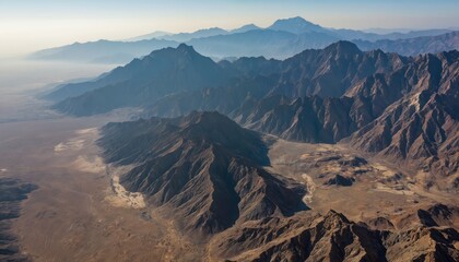 Aerial perspective rugged mountain ranges against dry desert valley under clear blue sky. Layers of mountains fade into distance creating sense of immense scale, natural beauty. Arid landscape offers