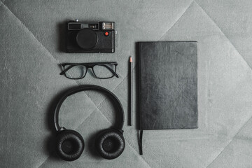 Notebook, pencil, headphones, glasses, camera, placed on a gray background.